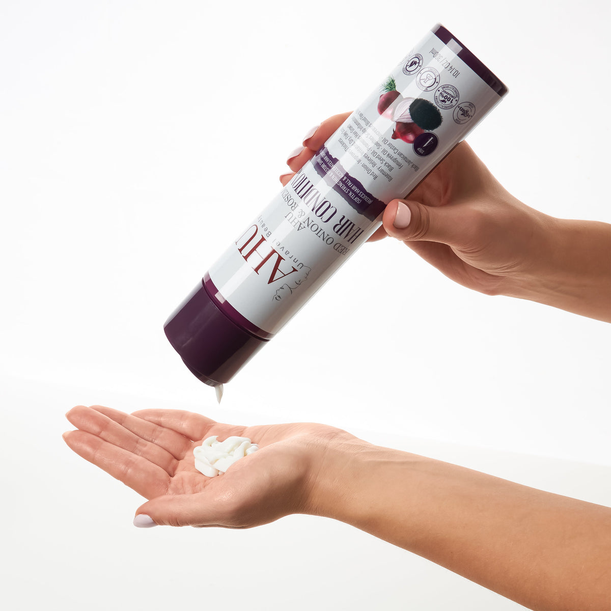 Hands holding the AHU Red Onion & Rosemary Hair Conditioner bottle and dispensing white cream onto an open palm