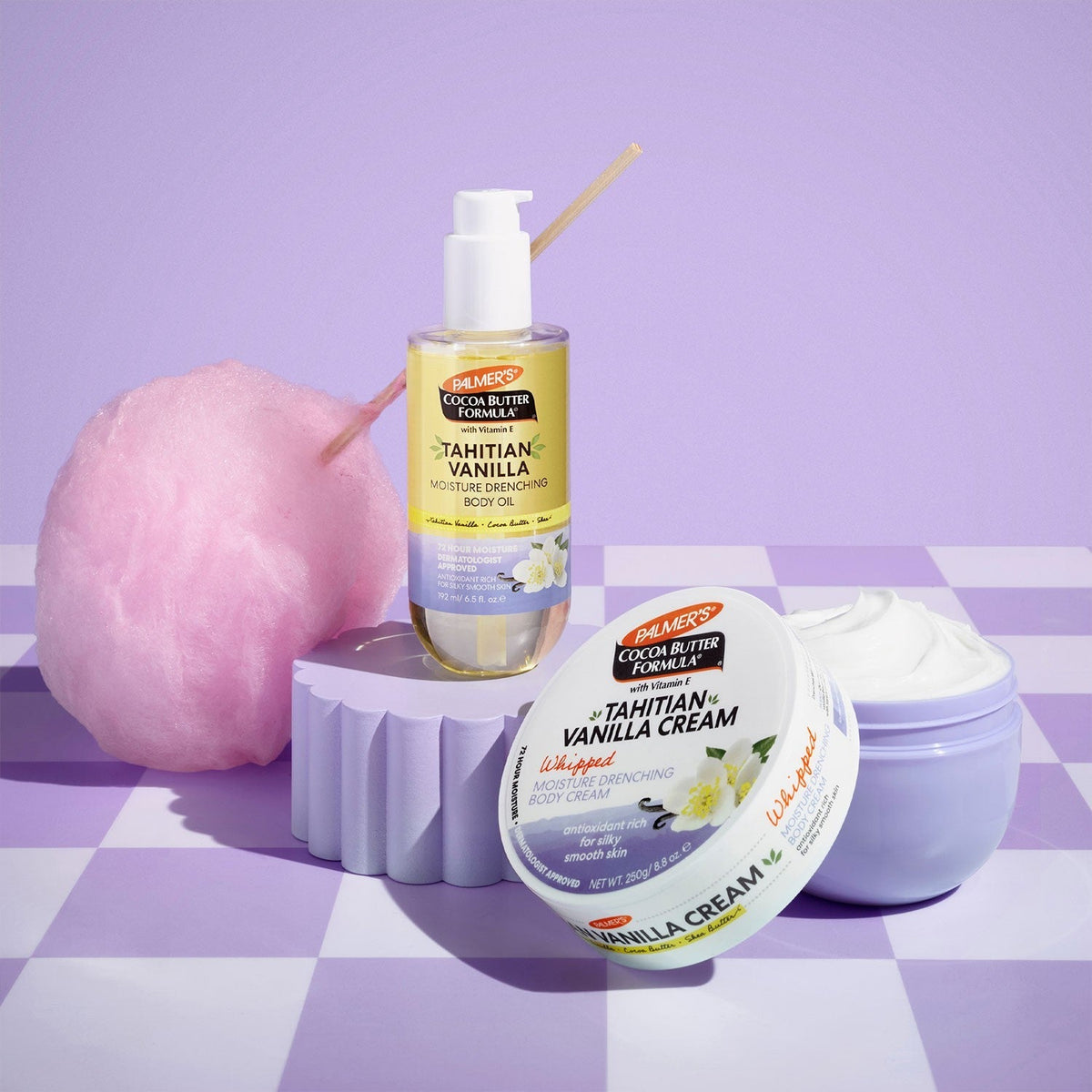 Tahitian Vanilla body oil and cream tub on a purple checkered surface next to pink cotton candy
