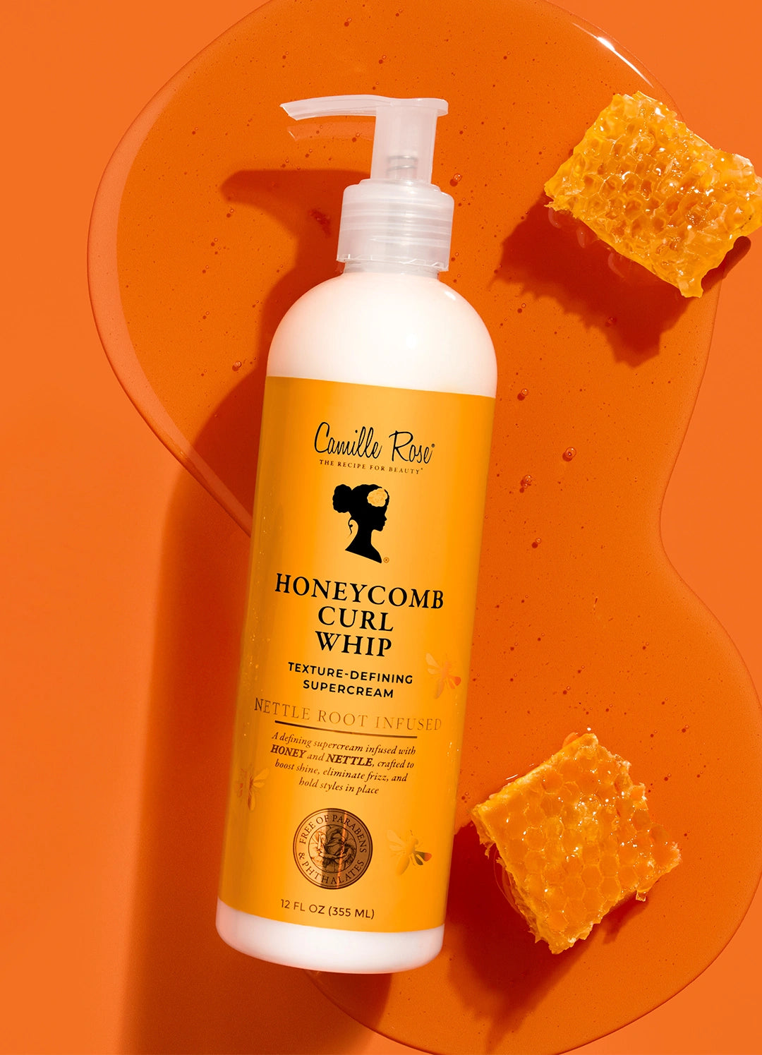 Honeycomb Curl Whip bottle lying on a pool of golden honey beside two pieces of honeycomb on an orange background