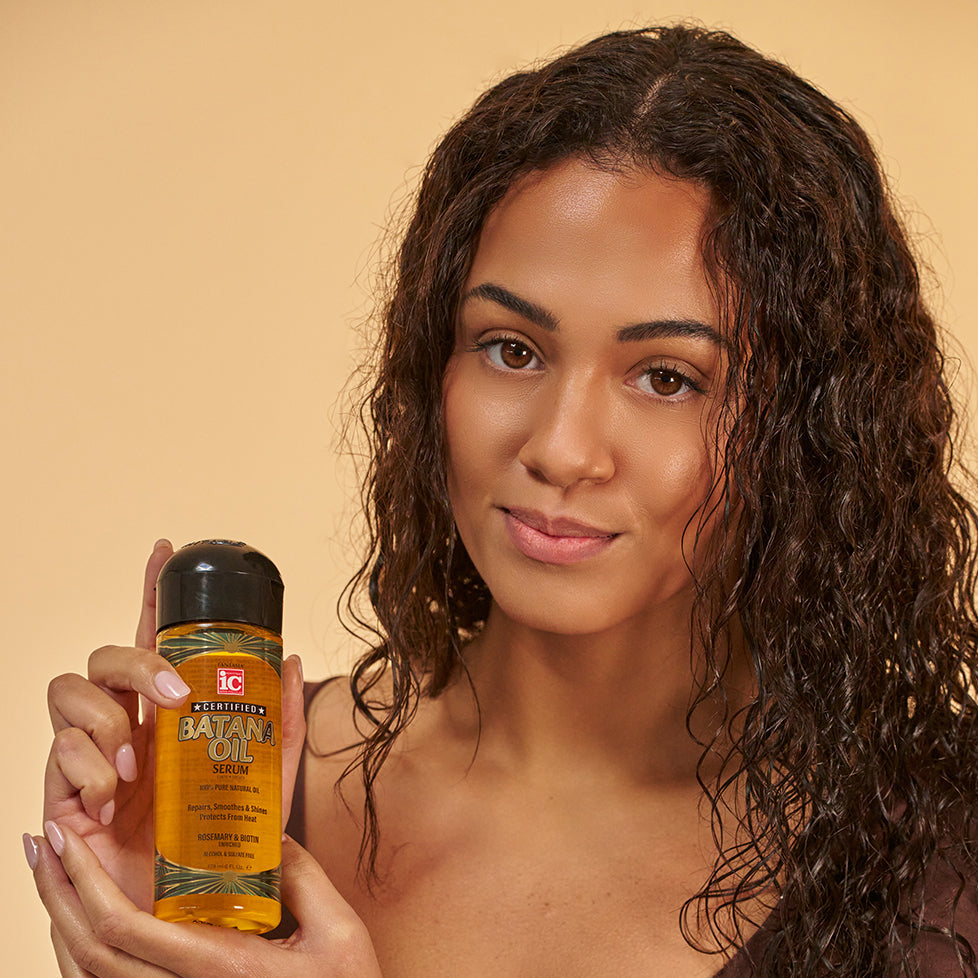 Model holding Fantasia IC Batana Oil Serum beside wet hair