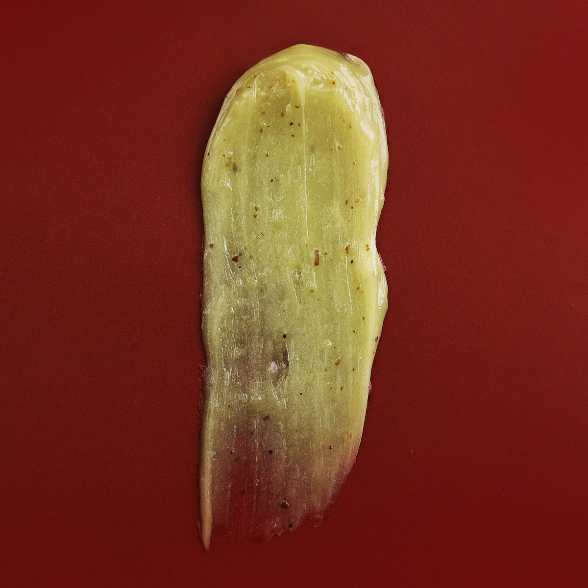 Smear of the pale green balm texture on a deep red background