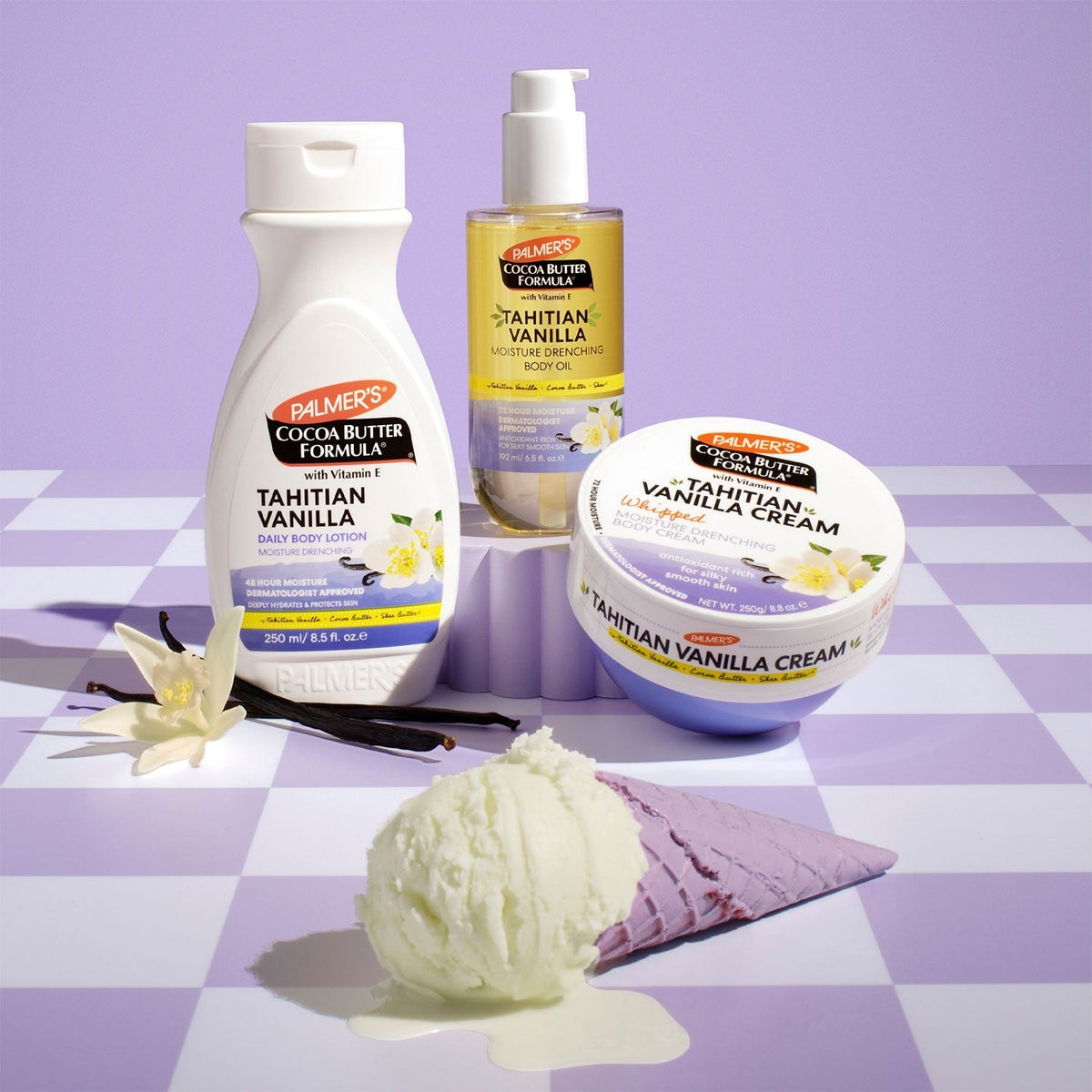 Tahitian Vanilla body oil, body lotion bottle and cream tub grouped on a purple checkered surface with vanilla pods and ice cream